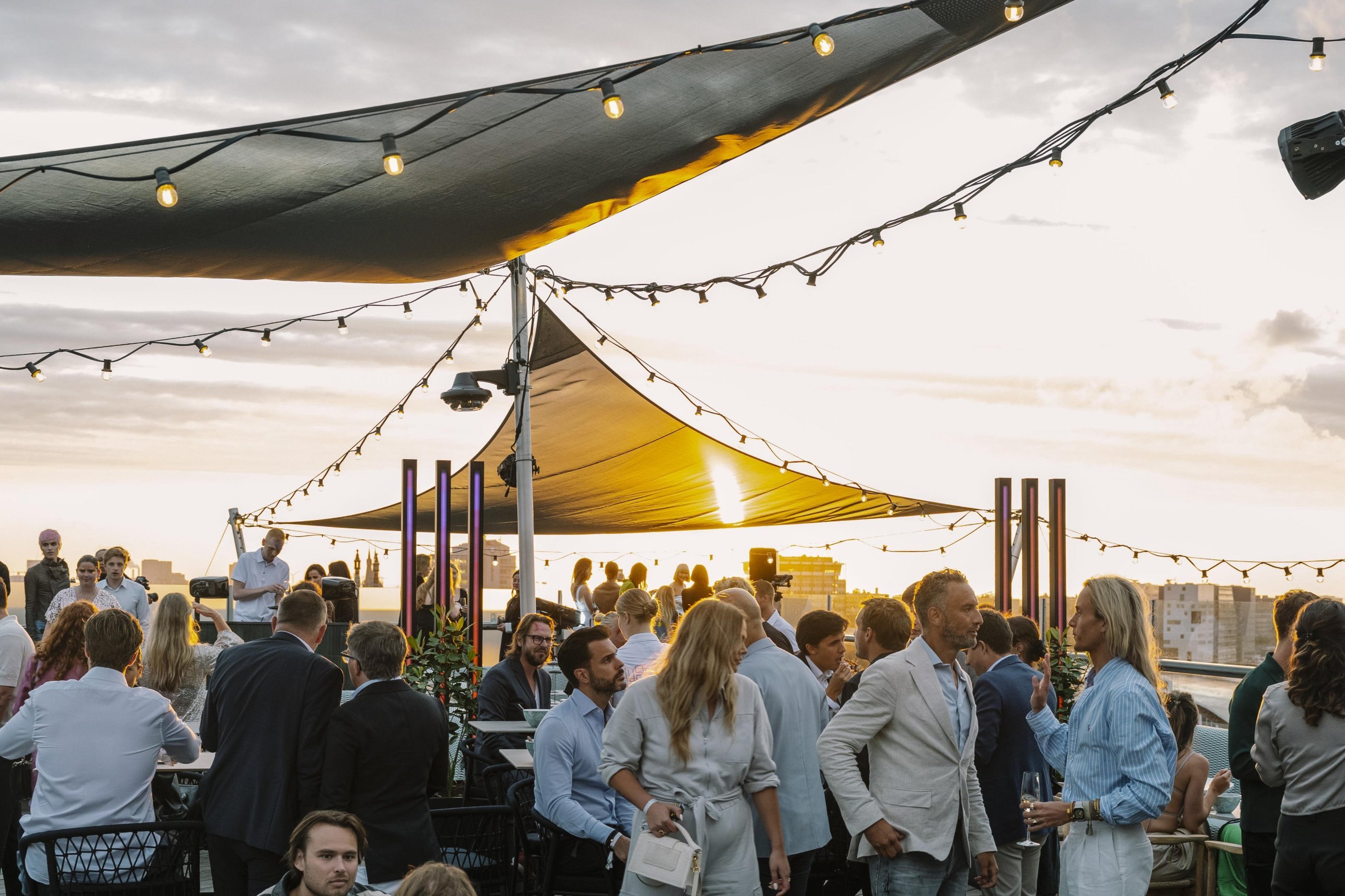 Rooftopfeest bij zonsondergang met lichtsnoeren en gasten